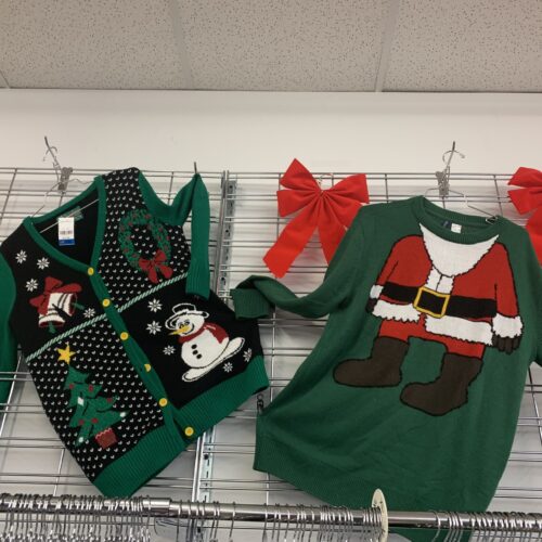 Des pulls d'hiver et de Noël sont accrochés au mur. L'un est vert avec un corps de Père Noël, l'autre avec un bonhomme de neige et des sapins.