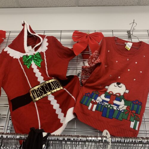 Des pulls de Noël accrochés au mur. Un Père Noël en rouge et un autre en rouge avec quelqu'un tenant des cadeaux.