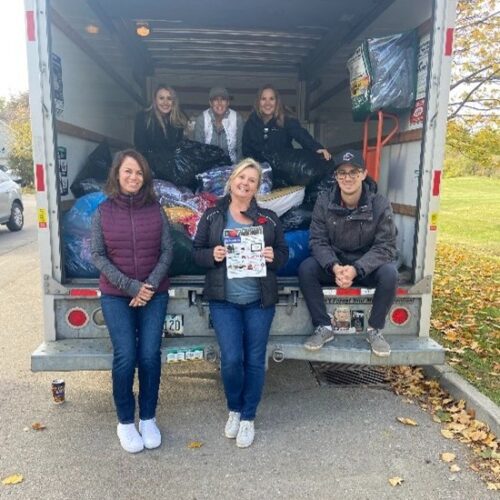 Groupe de personnes se tenant ensemble à l'arrière d'un camion ouvert rempli de vêtements et d'articles ménagers après une collecte de dons.