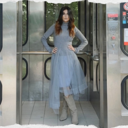 Camille wearing a grey dress standing in an elevator