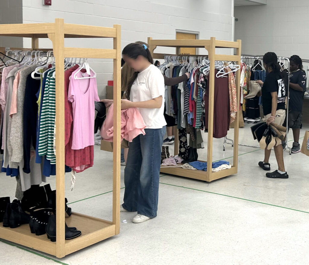 des portants à vêtements avec différents t-shirts, pulls, jeans et manches longues avec des jeunes femmes choisissant des articles