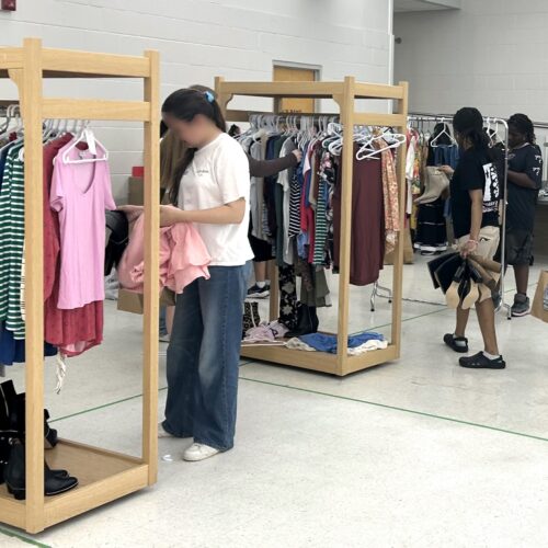 des portants à vêtements avec différents t-shirts, pulls, jeans et manches longues avec des jeunes femmes choisissant des articles de coupe carrée