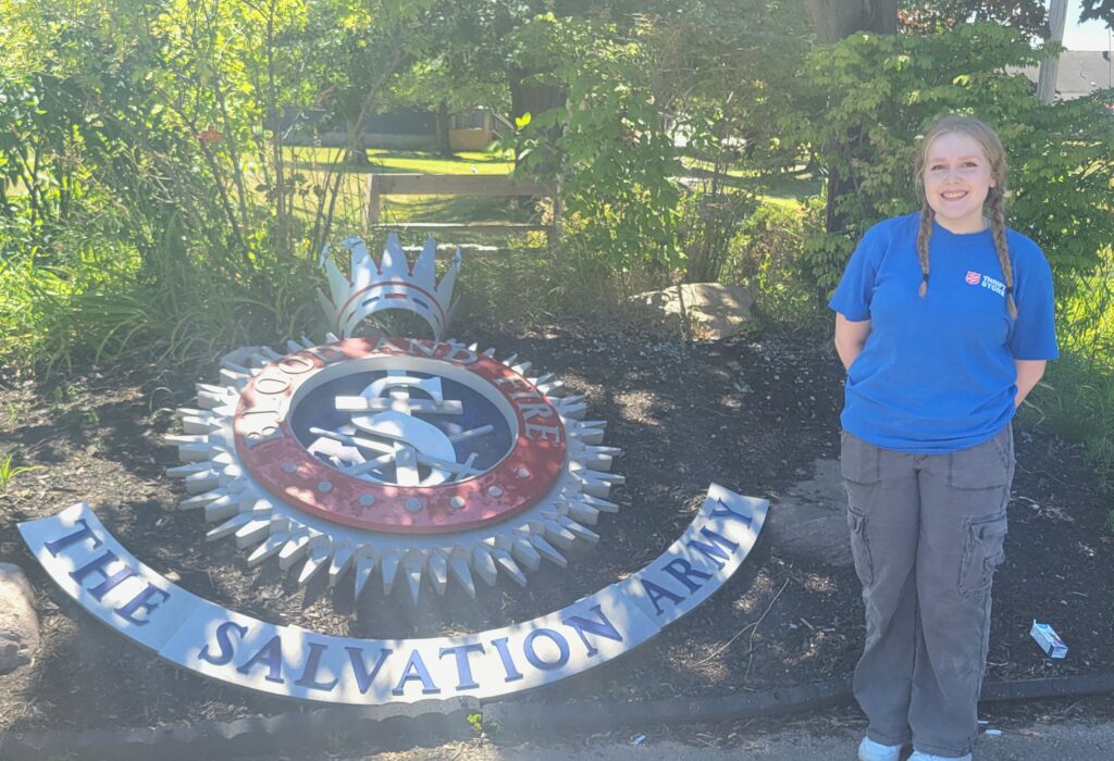 Sarah Jackman Streetsville employee standing in front of salvation army sig in the ground at camp