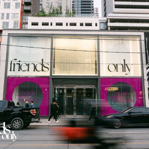 Devanture de Zara avec panneaux de vitrine indiquant « Réservé aux amis ». Des voitures passent et des passants devant le magasin.