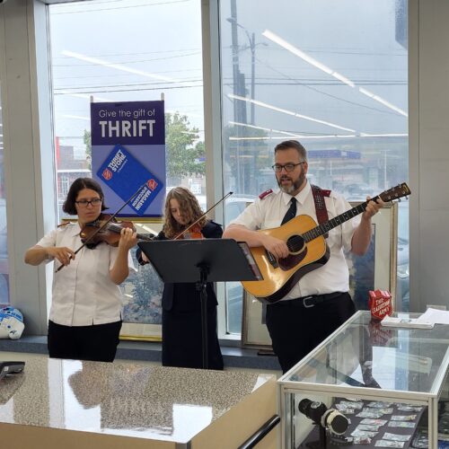 Un guitariste chanteur et deux violonistes debout jouant dans une friperie avec un pupitre carré