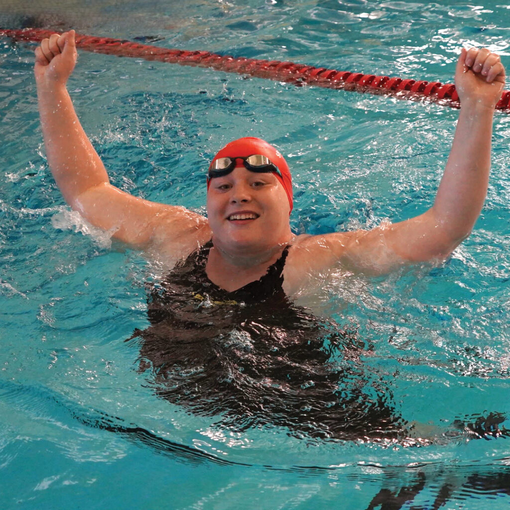 Casey hands up cheering from the swimming pool